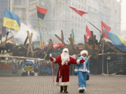 Personas disfrazadas de Santa caminan frente a una barricada en la Plaza de la Independencia de Kiev. ARCHIVO /