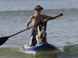 Una mujer rema al llevar a su perro en una tabla de surf. AP /