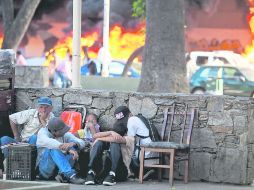 Cuatro habitantes de la capital venezolana se resguardan tras una barda mientras en la calle hay hogueras por bombas molotov. AP /