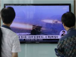 Dos hombres en Seúl observan en una televisión el nuevo operativo que usa artillería norcoreana. AP /