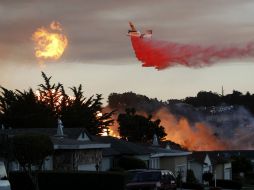 Un avión lanza agua con retardante de llama para consumir el fuego cercano a una zona residencial. AP /