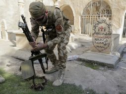Un militante iraquíe prepara su arma delante de una tumba en la aldea cristiana de Bakufa. AP / B. Janssen