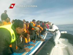 Guardacostas pasan a los indocumentados a un bote como parte de sus labores. EFE / Guardia Costera de Italia