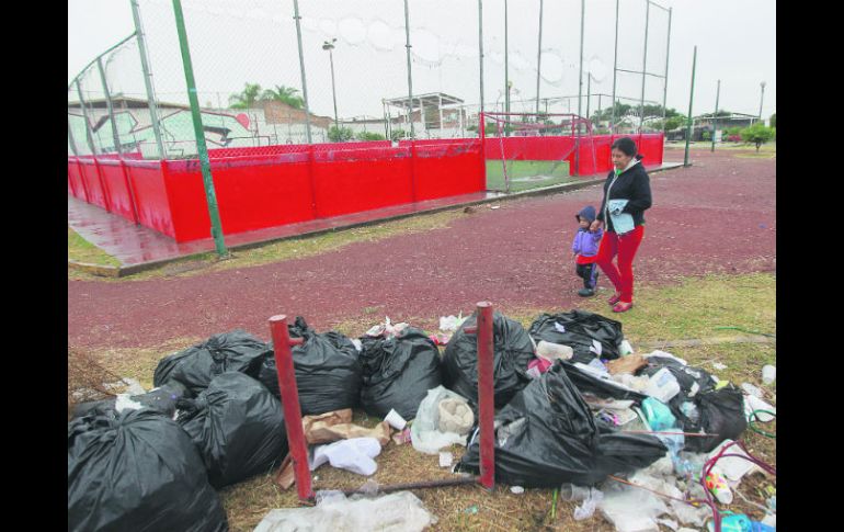 Isabel Montiel pasa con su nieto Samuel frente a varias bolsas de basura abiertas que se encuentran en una unidad deportiva de Tonalá. EL INFORMADOR / F. Atilano