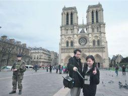 Dos turistas se toman una fotografía en la catedral de Notre Dame, mientras un soldado francés vigila la zona. AP /