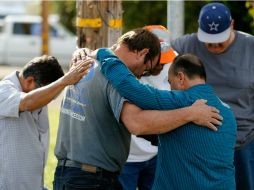 Un grupo de hombres reza afuera de la escena del crimen en memoría de las víctimas. AFP / S. Haffey