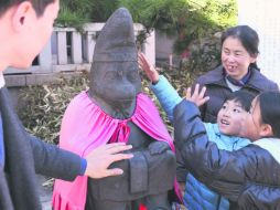 Una familia toca la estatua de un mono guardián a la entrada de un templo de Tokio como parte de rituales de Año Nuevo. AP /