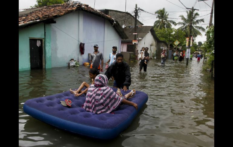 Un sujeto transporta a varias niñas con la ayuda de un colchón inflable hacia un lugar seguro en medio del agua. AP / E. Jayawardena