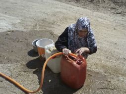 Una mujer llena un recipiente con agua; la escasez de insumos está llevando a los pobladores a la desesperación. AP /