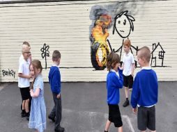 Varios pequeños observan la pintura, en la que se aprecia a una niña jugando con una llanta en llamas. EFE / N. Munns