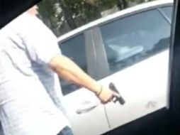 El sujeto, de camisa blanca y pantalón oscuro, amedrenta a otro conductor con un arma, sin que este descienda de su vehículo. YOUTUBE / PolakasTV