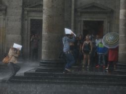 Tapatíos se protegen de la intensa lluvia bajo la parte frontal del Teatro Degollado. EL INFORMADOR / R. Tamayo