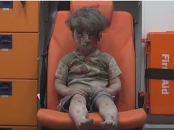 El niño, con pantalón y camiseta corta, observa a las cámaras desde el asiento naranja de una ambulancia. ESPECIAL / AMC