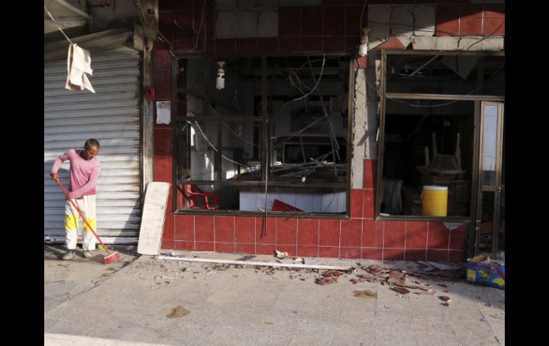 El propietario de un negocio limpia los vidrios rotos y pedazos de ladrillo que quedaron tras el estallido. AP / K. Kadim