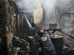 Bomberos apagan el fuego en las casas dañadas por los ataques de las fuerzas leales al Gobierno sirio. EFE / M. Badra