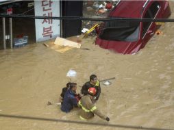 Bomberos ayudan a una mujer a salir de una zona afectada por las inundaciones. AP / L. Sang-hyun