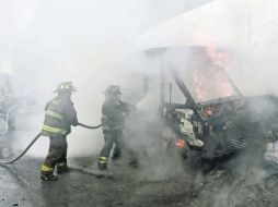 Riesgo. Bomberos apagan las llamas de un microbús que delincuentes usaron para obstruir el operativo de la Marina. AFP /