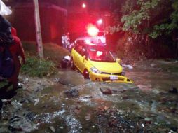 Bomberos apoyan a un taxi varado este lunes tras la lluvia que duró toda la madrugada. ESPECIAL /