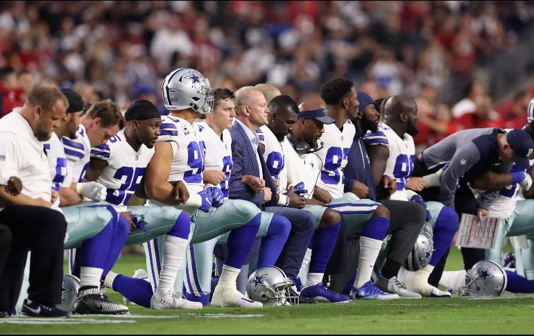 Sin dejar de sujetar los brazos, los Vaqueros se pusieron de pie cuando la bandera de Estados Unidos se desplegó en el terreno. AFP / C. Petersen