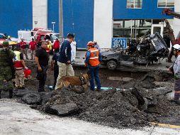 Bomberos y elementos de Protección Civil recuperan el vehículo que cayó en el socavón, en el cual que viajaba la mujer. EFE