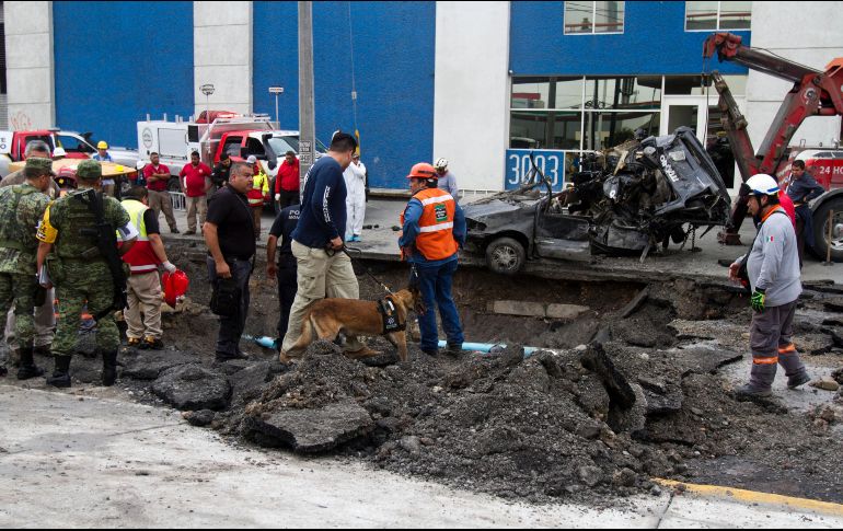 Bomberos y elementos de Protección Civil recuperan el vehículo que cayó en el socavón, en el cual viajaban cinco personas. EFE