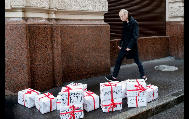 Un activista opositor porta una máscara de Putin mientras pasea por las cajas de regalo con títulos que leen “juicio”, “renuncia” y otros. AFP/M. Zmeyev