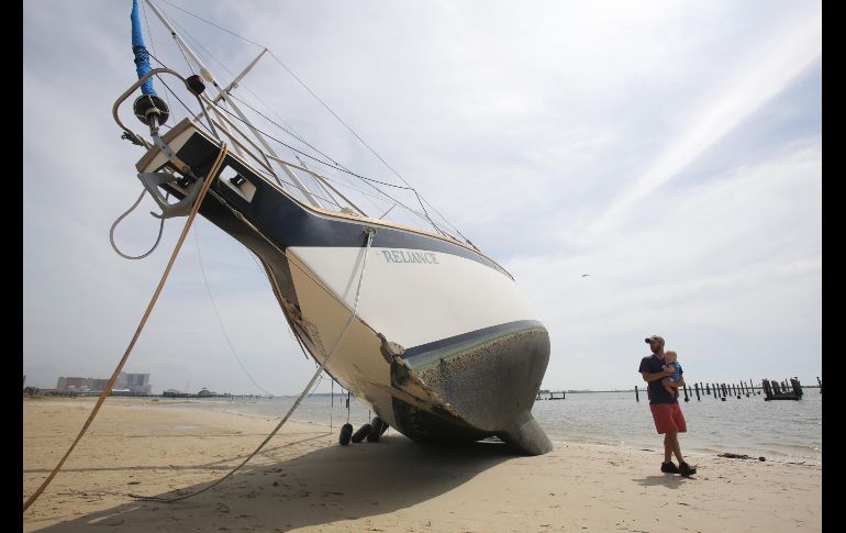 Un hombre y su hijo pasan junto a un bote arrojado a la playa por efectos del huracán 