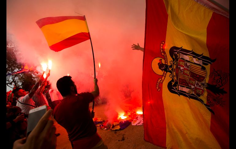 Manifestantes de extrema derecha sostienen banderas españolas de la época previa a la constitución mientras queman 
