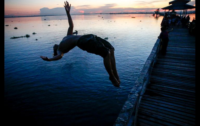 Un niño se avienta al agua desde un puente, que abarca más de un kilómetro sobre el río Taungthaman, en la capital de Birmania. Es considerado el puente de madera más largo del mundo. EFE / L. Bo bo