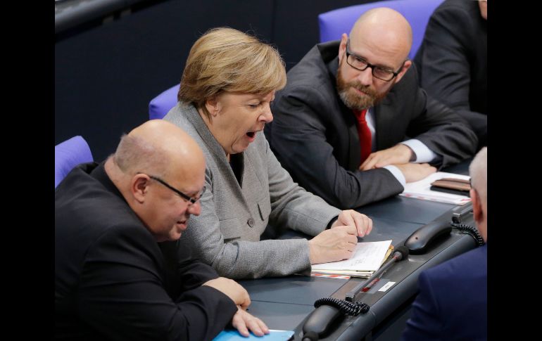 La canciller alemana Angela Merkel bosteza durante una plática con el jefe de su staff Peter Altmeier y el secretario general de su partido Peter Tauber, en la sesión constituyente del nuevo Parlamento alemán en Berlín. AP/F. Ostrop