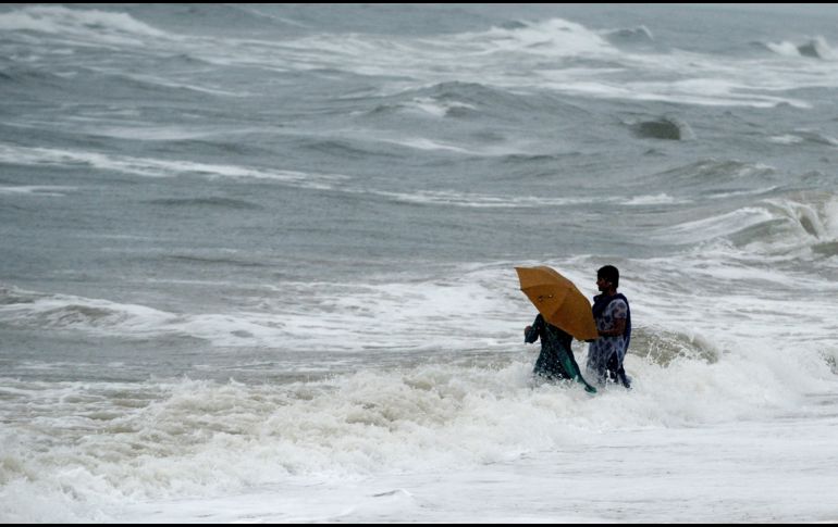 Habitantes caminan por el agua en la playa de Chennai, India, durante la temporada de monzón. AFP/A. Sankar