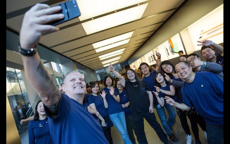 Un cliente (c) posa para una selfi con trabajadores de una tienda Apple luego de comprar su celular en Pekín, China.