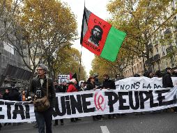 Manifestantes avanzan detrás de una manta donde se lee: 'El Estado arruina a las personas'. AFP/C. Archambault