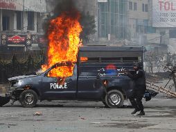 Un miembro de las fuerzas de seguridad dispara contra los manifestantes cerca de una patrulla en llamas. AP/A. Naveed