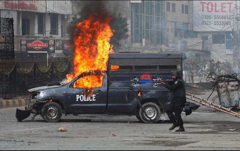 Un miembro de las fuerzas de seguridad dispara contra los manifestantes cerca de una patrulla en llamas. AP/A. Naveed