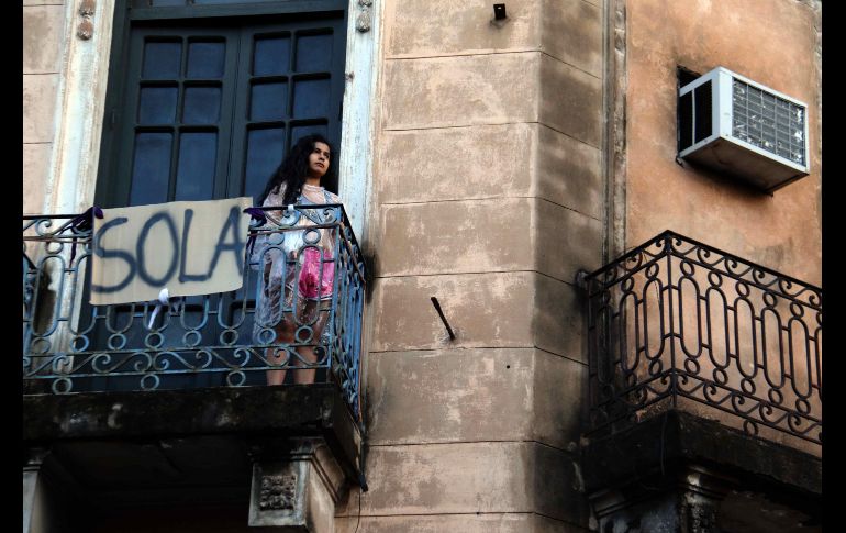 Una chica observa el aspecto de la manifestación desde su balcón, junto a un cartel con la palabra 