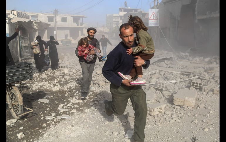 Sirios pasan entre escombros luego de un ataque aéreo en la población bajo contro de los rebeldes de Beit Sawa. AFP/A. Almohibany