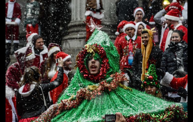 Un sujeto viste de un auténtico árbol de navidad con adornos en rojo a su alrededor. AFP / S. Keith