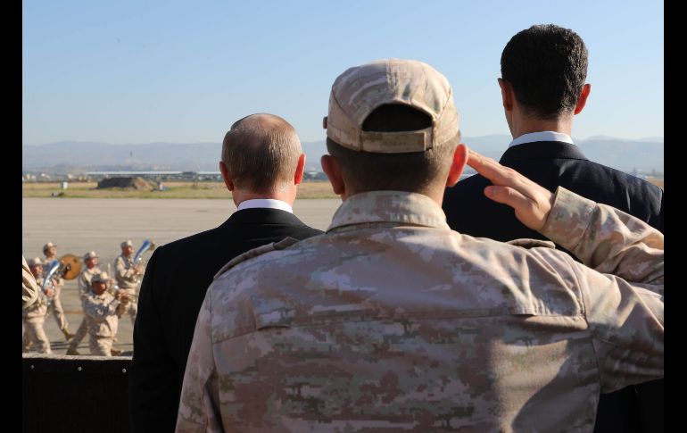 El presidente ruso Vladimir Putin (i) y el mandatario sirio Bashar al-Assad (d) inspeccionan un desfile militar en su visita a la base aérea rusa en Hmeimim, en el noroeste de Siria. AFP/M. Klimentyev