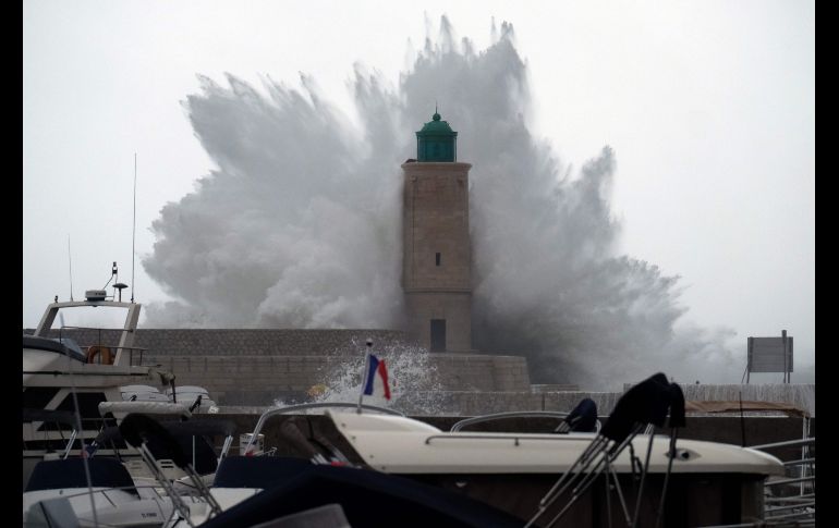 Una ola se estrella en un embarcadero y un faro en Cassis, Francia, por el efecto de la tormenta 