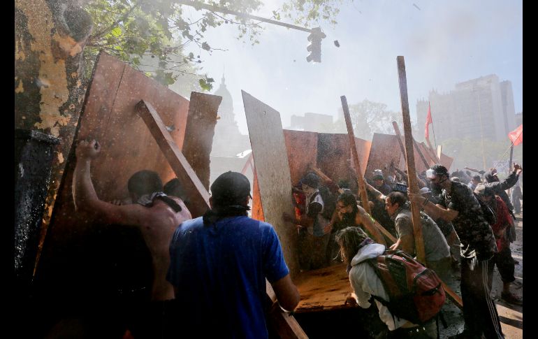 Manifestantes se cubren durante enfrentamientos con policías en Buenos Aires, afuera del Congreso donde se debate la polémica reforma de pensiones impulsada por el Gobierno. AP/V. Cavaino