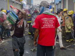 Varias personas colaboran en el retiro de mercancía durante las tareas de extinción del incendio. EFE/J. Torres