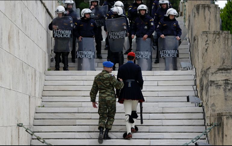 Un militar ayuda a un guardia presidencial a moverse de su posición mientras manifestantes se acercan a la Tumba del soldado desconocido, afuera del Parlamento en Atenas, Grecia. Sindicatos protestan contra mayores medidas de austeridad. AP/T. Stavrakis