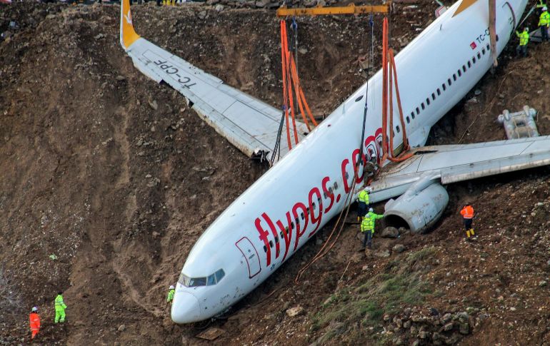 Técnicos observan mientras grúas levantan el avión de la aerolínea Pegasus que se salió de la pista hacia un acantilado el pasado 15 de enero, tras aterrizar en el aeropuerto de Trabzon, en Turquía. AFP/Dogan News Agency