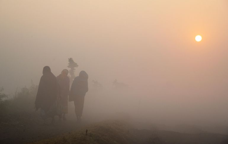Trabajadores caminan por un campo agrícola en una mañana con neblina en Calcuta, India. AFP/D. Sarkar