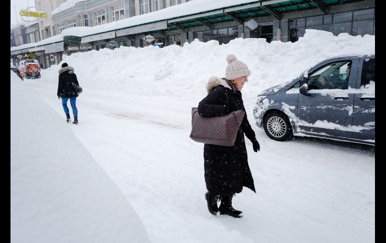 Gente camina por una calle luego de que se hiciera la nieve a los lados.