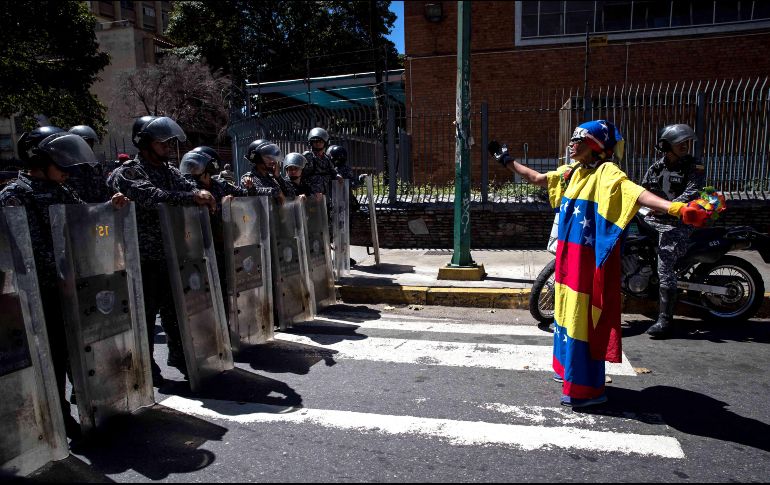 Un manifestante envuelto en la bandera venezolana levanta sus brazos frente a policías en Caracas. Los cuerpos de seguridad dispersaron una manifestación en recuerdo a Óscar Pérez, el ex policía muerto en un operativo del gobierno. EFE/M. Gutiérrez