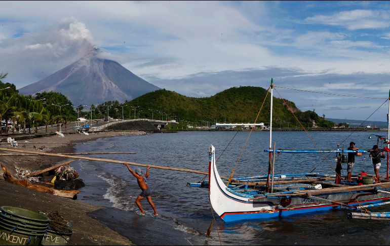 Pescadores trabajan en las inmediaciones del volcán, que emite una larga columna de humo. AP/B. Marquez