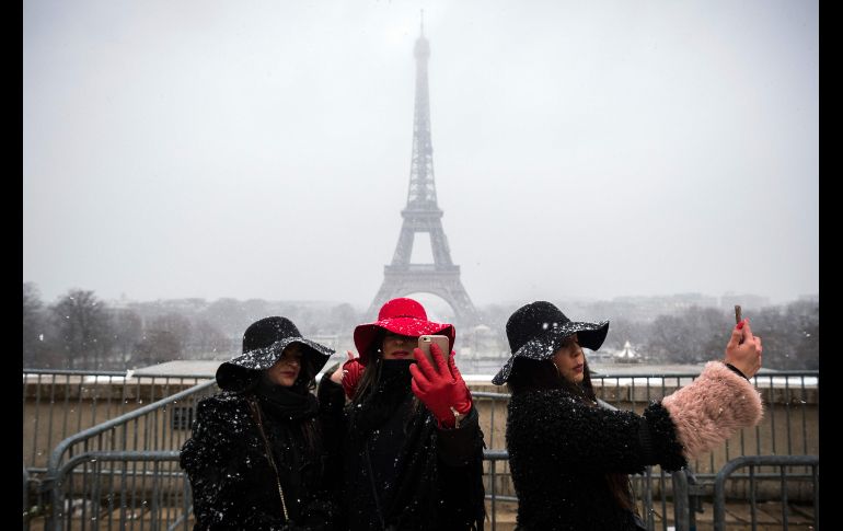 Mujeres posan para fotos frente a la torre Eiffel, en París, mientras nieva. AFP/L. Bonaventure