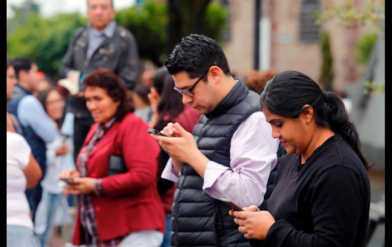 Personas revisan sus celulares mientras aguardan la instrucción de volver a los inmuebles. AFP/U. Ruiz